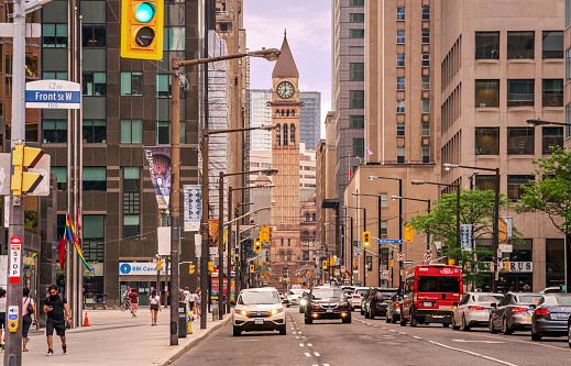 Toronto, Canada - 06 05 2021: Summer view along Bay Street in downtown Toronto with Old City Hall, Richardsonian romanesque civic building of 1899 with clock tower and gargoyles in background.