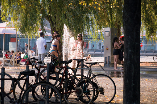 Toronto, Canada - 08 29 2021: Torontonians in downtown Toronto having fun on the Sugar Beach beside the fountain under green branches of a willow tree with a bicycle stall in the foreground.