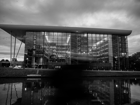 Strasbourg, France - Sep 19, 2017: Defocused silhouette of cyclist - Side view of Agora building at dusk near Ill river - large wide glass building modern architecture of Council of Europe premises