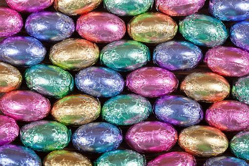 Angled close up top view image of plastic easter eggs being filled with chocolates before easter egg hunt. It is a fun activity for children who search for eggs and get the chocolates.