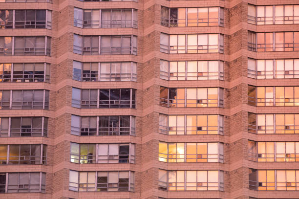 Urban geometry. Rows of large windows with various curtains, shutters, blinds, jalousies in a bricky wall of residential condo high-rise building.