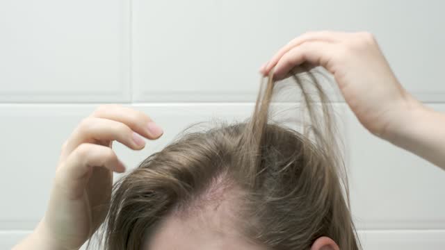 Woman touching her hair close-up on white tiles background, hair loss concept.