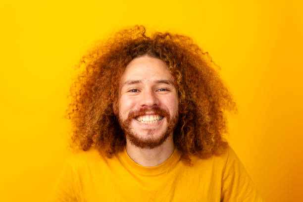 Joyous man with curly hair smiling widely against a monochrome yellow background.