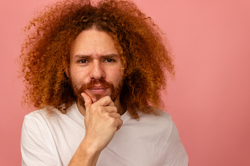 Curly-haired man looks pensive with hand on chin.