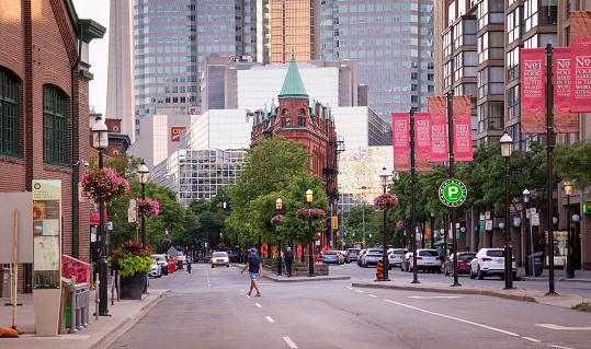 Toronto, Canada - 07 21 2020: Summer evening view along Front street with colorful flowerbeds, green trees, and Gooderham flatiron building before high-rise buildings of Toronto financial district in the background.