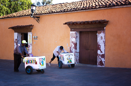 Oaxaca, Mexico: Two roving ice cream vendors push their carts past a colorful building in downtown Oaxaca.