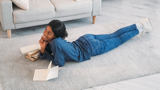 Creative writer. Diary leisure. Thoughtful dreamy inspired happy young author woman taking notes in journal on floor carpet in home living room.