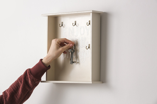 Woman is hanging keys on the key holder on the wall, domestic living concept