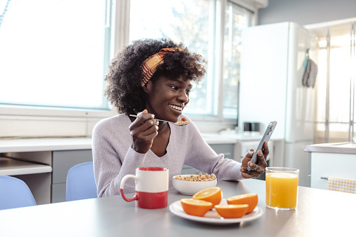 Photo of African American woman using smart phone and surfing the Net while having breakfast