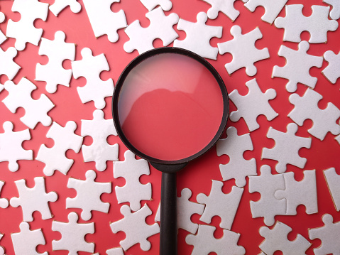 Top view white puzzle and magnifying glass on a red background.