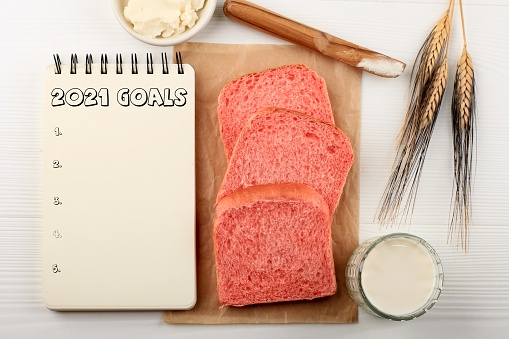 New Year Diet Goals List 2021 with Open Blank Notebook Written in Handwriting about Plan Listing of New Year Goals and Resolutions Setting with Pink Healthy Bread. Flat Lay Style Concept.