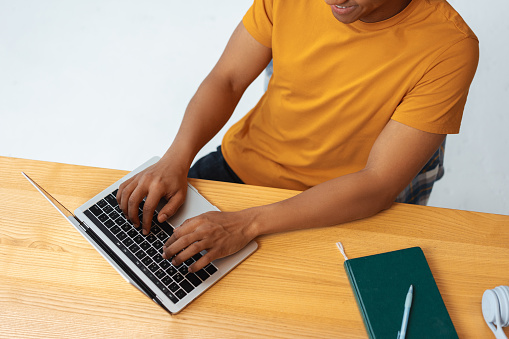 Portrait of smiling confident Latin man, programmer, copywriter typing on keyboard, using laptop while sitting at workplace top view. Startup planning concept