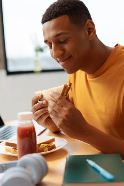 istock Handsome Latin man holding sandwich, eyes closed enjoying eating while sitting in kitchen at home 2021428923