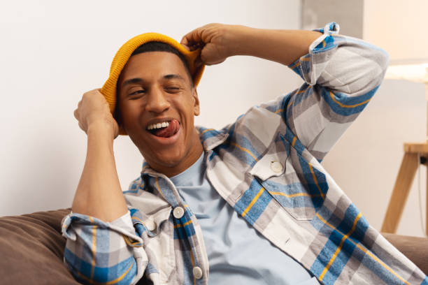 Handsome African American man wearing modern yellow hat fooling around, showing tongue