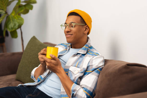 Positive authentic African American man wearing stylish yellow hat, holding yellow cup of coffee