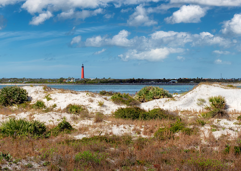 Beach sand dunes in sunny day and Lighthouse Ponce de Leon Inlet in New Smyrna beach, Florida.
