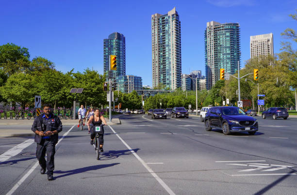 peatones y ciclistas cruzando la calle en lake shore boulevard west y el cruce de la avenida strachan frente a nuevos edificios residenciales de gran altura con fachadas de vidrio - ontario spring bicycle city life fotografías e imágenes de stock