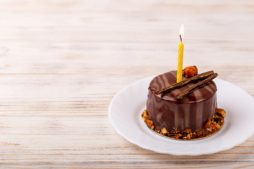 Delicious chocolate cake with candle on plate on white wooden background. Caramel glaze and decoration add appeal and desire