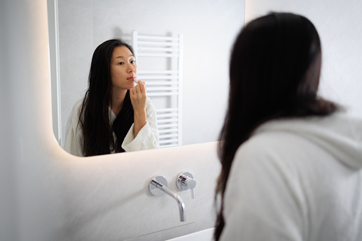 Asian Lady in bathroom mirror after shower, Applying lipstick