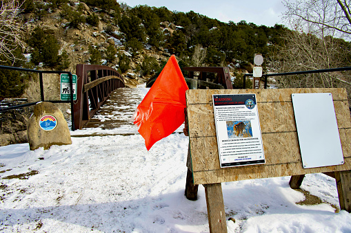 Buena Vista, Colorado, USA - February 10, 2024: A sign and bright orange flag posted by Colorado Parks and Wildlife warns hikers of recent mountain lion activity near the Whipple Bridge that crosses the Arkansas River and intersects the Arkansas River Trail.