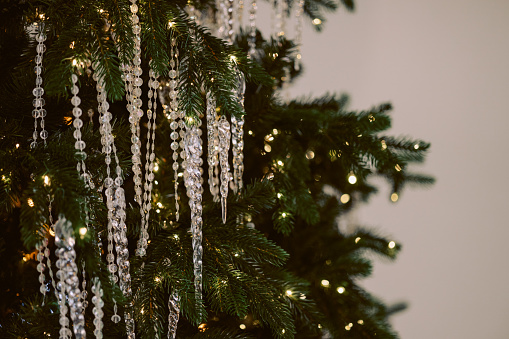 Close-up of a Christmas tree, adorned with shimmering crystal garlands. The decorations cast a magical glow on the dark green pine needles. Concept for holiday decorations and festive atmosphere.
