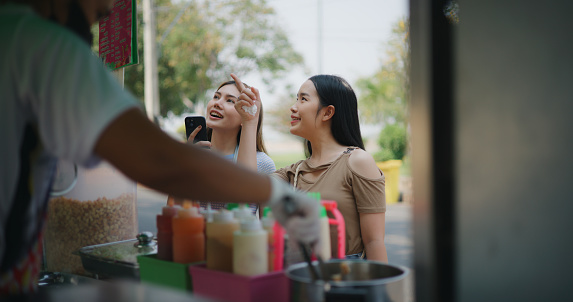 Cheerful Young tourist woman talking and smiling with female friend while waiting after ordering at snack shop, Delicious Local food in rural