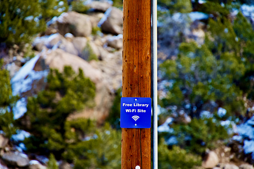 Buena Vista, Colorado, USA - February 10, 2024: A metal sign posted on a telephone pole in a public park tells visitors there is “Free Library Wi-Fi Site” available for use in this natural area.