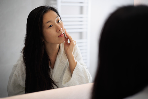 Beauty care. Asian Lady in bathroom after shower, make up remove with cotton pads