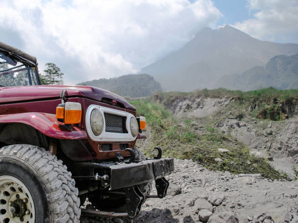 A red jeep parked on a rocky area with Mount Merapi in the background