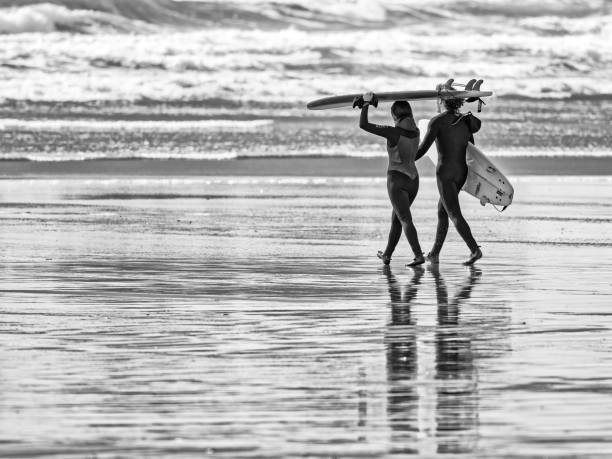 The Pacific Rim National Park on Vancouver Island on April  16, 2023:   Young couple entering the water for a surfing session at Pacific Rim National Park on Vancouver Island at sunset, British Columbia