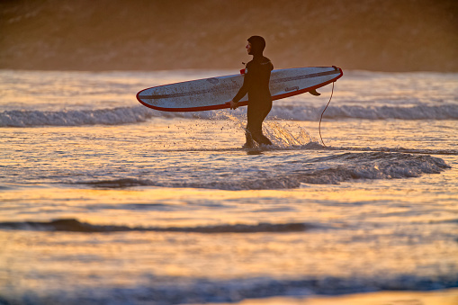 An image of an unrecognizable long-boarder in silhouette in Seal Beach, California.