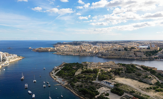 Discover Sliema and Valletta in Malta overlooking the Mediterranean Sea with boats sailing on the blue ocean Surface. Manuel Island seen in the middle. Seen a sunny day.