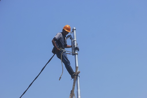 Jakarta, 27 Sept 2023:  Electricians Installing power cable on monopole to distribute the power line to the house nearby.