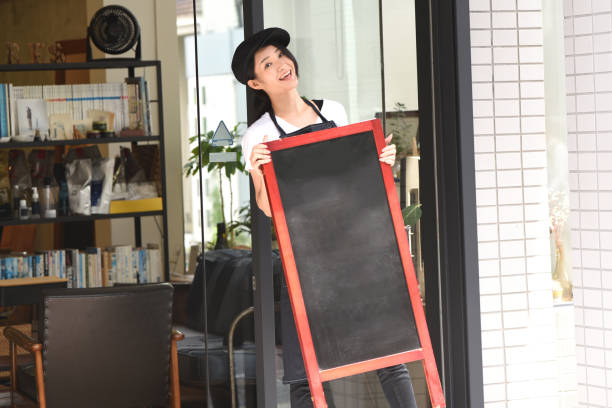 a young asian female clerk is setting up an easel sign in front of the restaurant to attract customers. - soda jerk imagens e fotografias de stock