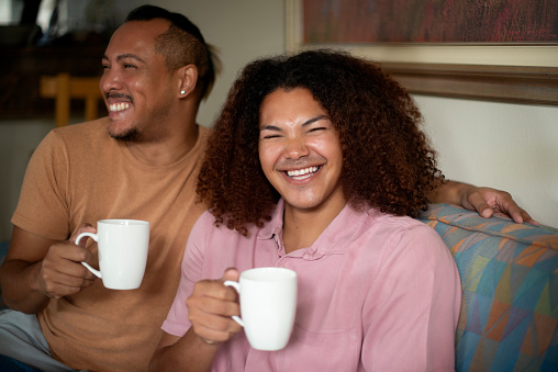 Happy couple, coffee and relax in living room for bonding, chat or story with love and care at home. People in relationship on sofa, support and trust with drink for commitment and communication