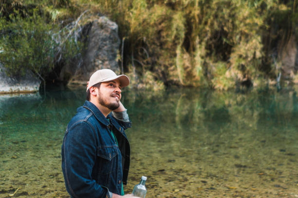 Contemplative man with water bottle by a clear river.