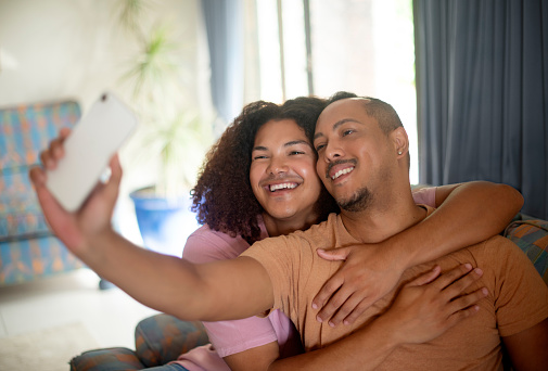 Selfie, happy and gay couple hug on sofa in home for bonding, lgbtq relationship and relax together on weekend. Queer, love and men take picture for social media, online post or memory in living room
