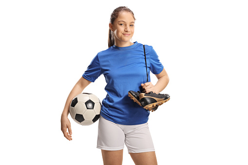 Teenage female football player holding a soccer ball and cleats isolated on white background