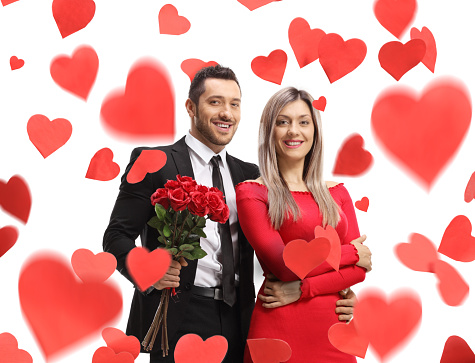 Couple with a bunch of red roses standing under confetti hearts isolated on white background