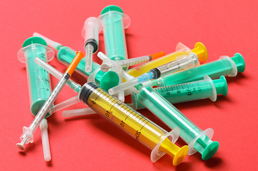 Top view of a pile of medical syringes and insulin syringes with needles at red background with copy space. Injection treatment concept.