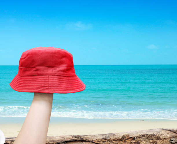 istock red bucket hat in hand with beach background 2022142421