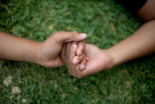 Closeup, couple and holding hands on grass for care with bonding, relax and partnership in backyard of home. People, love and support on lawn in garden of house or park with kindness and relationship
