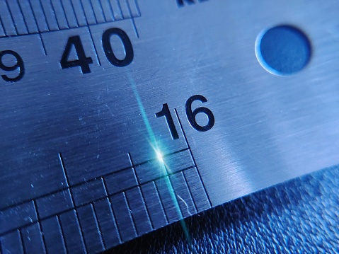 The number sixteen or 16 on a glowing metal ruler. Steel Ruler shot with light effects.