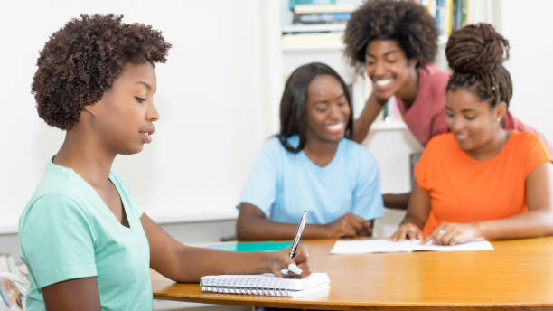 istock Working black female student at desk with group of learning african american students 2022177898