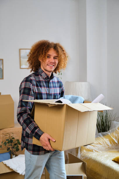 Latin man holding a moving cardboard box to settle in his new home. stock photo