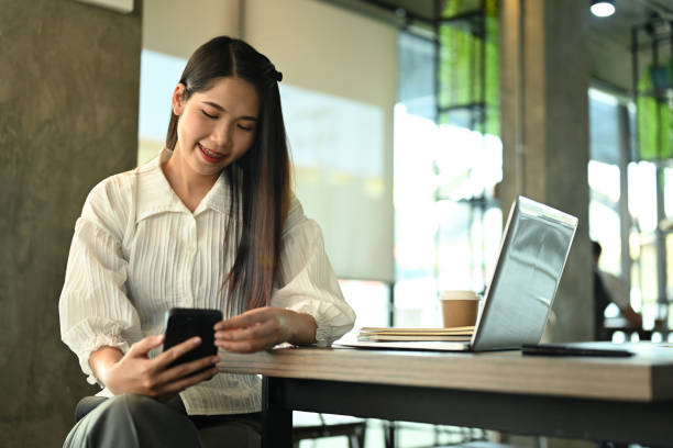 istock Smiling businesswoman using mobile phone while sitting at table with laptop during remote work at coffee shop 2022193557