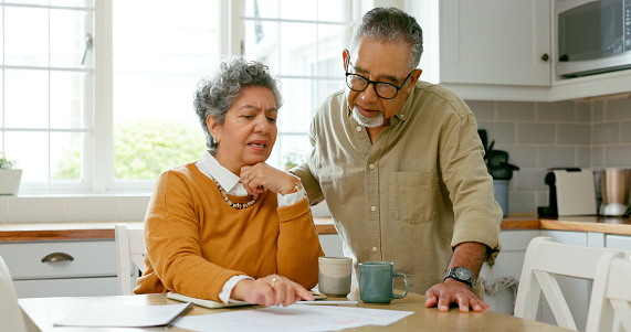 Documents, discussion and senior couple in kitchen for bills, debt or mortgage payment at home. Conversation, paperwork and elderly man and woman in retirement planning pension funds at house.