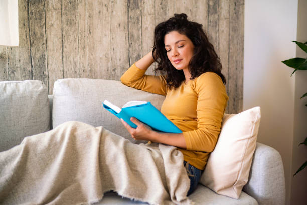 istock A woman is reading a book while sitting on a comfortable couch 2022201034