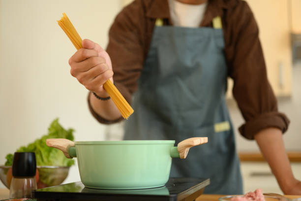 istock Young man in apron putting raw spaghetti pasta into pot with boiling water 2022203710