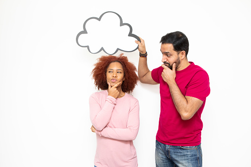 Couples with ideas and making decisions concept: Mid-adult man holding a blank cloud bubble for your message above a young woman. They both have doubtful expressions.